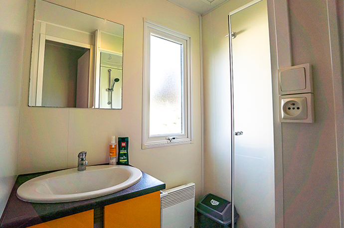 L’espace cuisine et séjour avec une table, chaises et banquette convertible 2 couchages du mobil-home Le Brand 6 personnes, en location au camping le Médiéval proche de Colmar